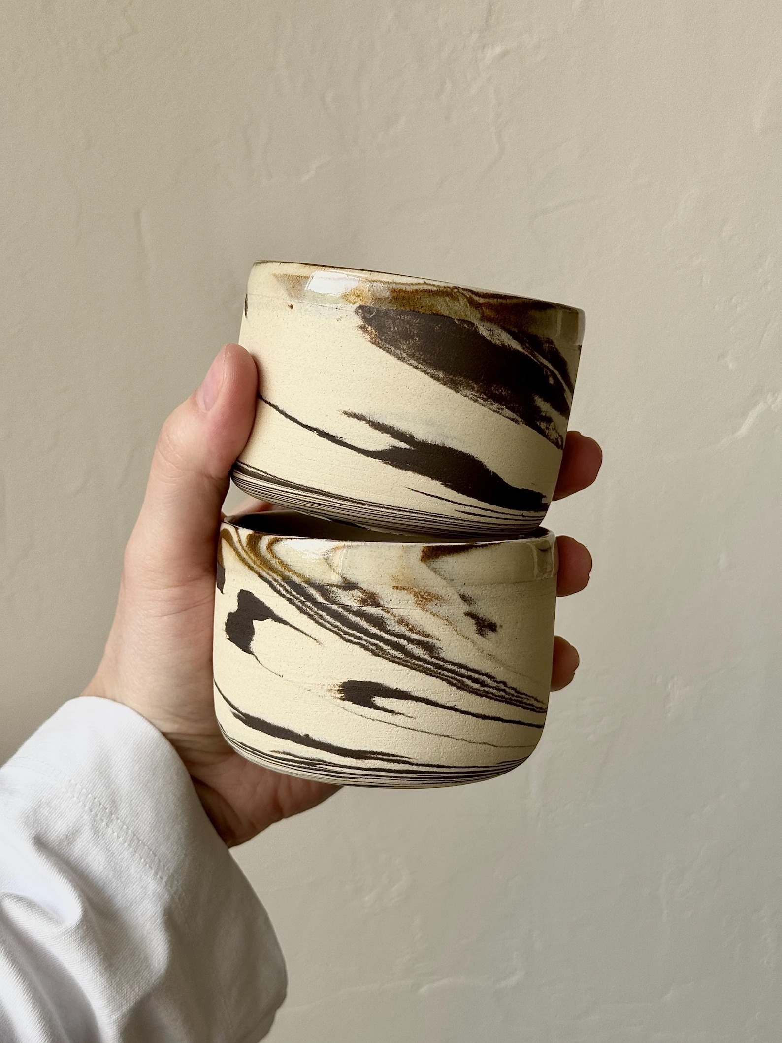 Hand holding two marbled cream-and-brown studio ceramic cups