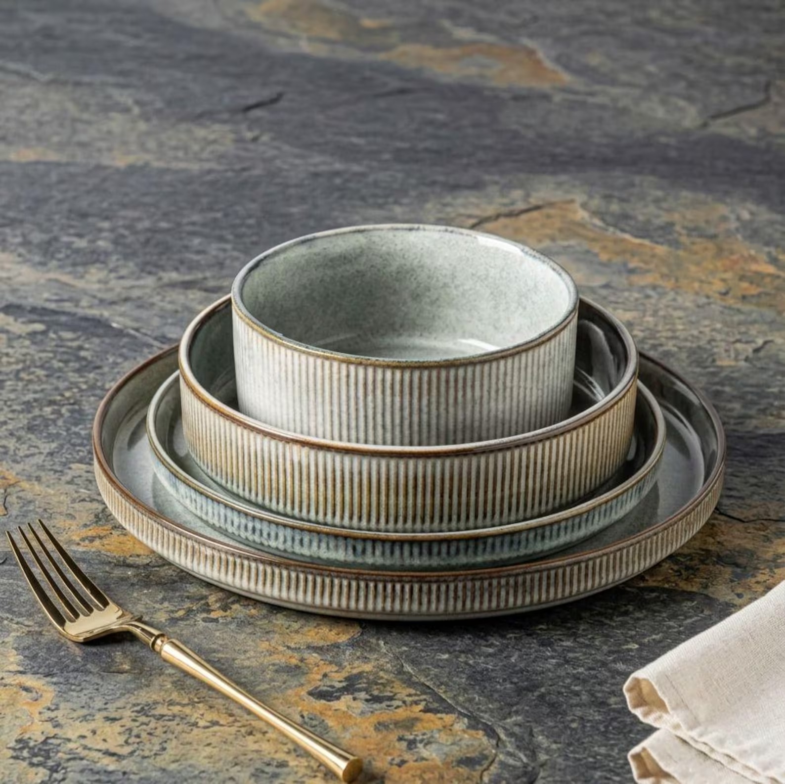 Ribbed sage-green stoneware dinner set stacked on a slate surface